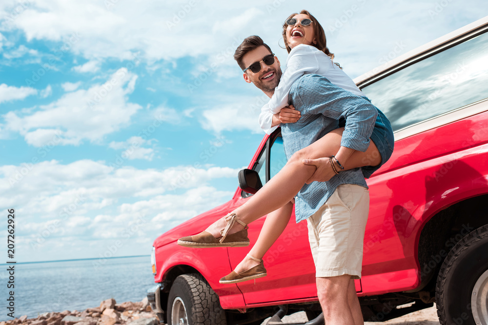 young man piggybacking his excited girlfriend near red jeep