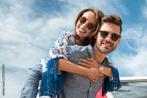 handsome man in sunglasses piggybacking his smiling girlfriend photo
