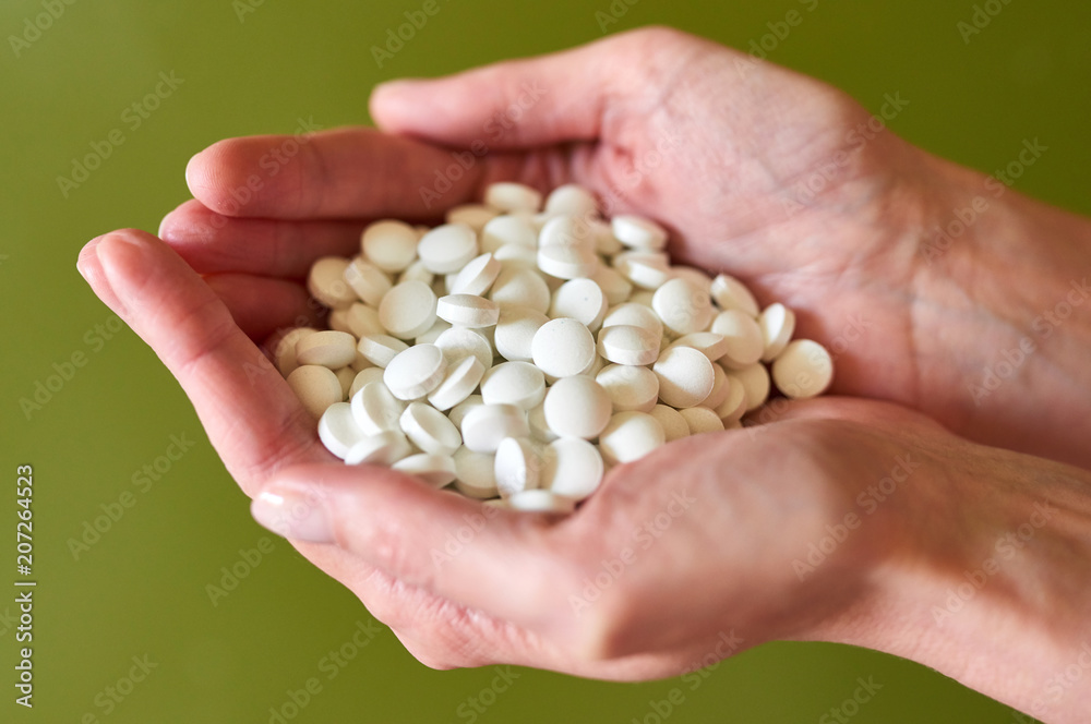 Woman's holding cupped hand full of pills over green background, view from above Woman's holding cupped hand full of pills over green background, view from above