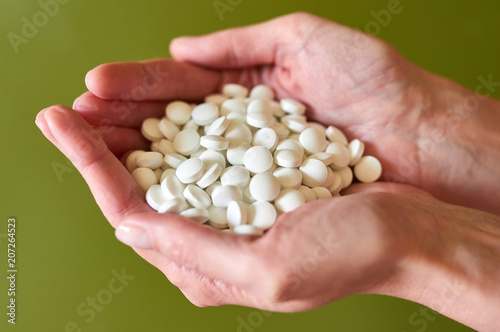 Woman's holding cupped hand full of pills over green background, view from above