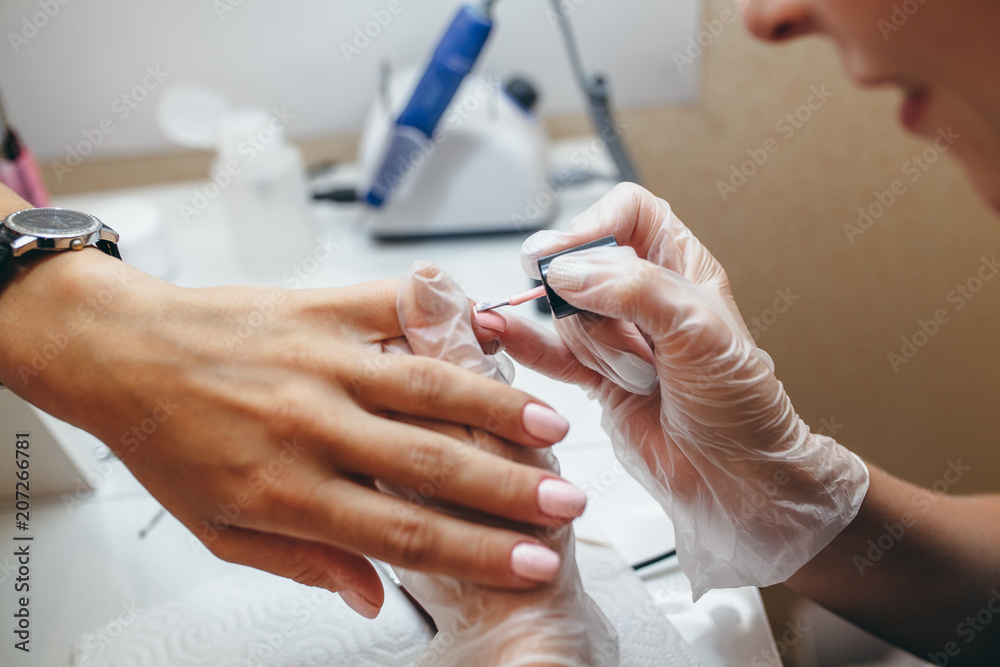 Obraz premium Woman in a nail salon receiving a manicure by a beautician.Female hands doing nail polish in pastel pink color