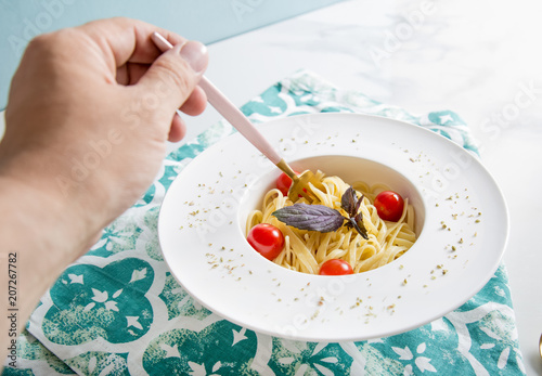 Traditional italian pasta with tomatoes and basil in plate with fork and hand