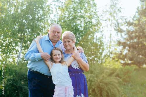 family, love, generation and people concept - happy smiling grandmother, grandfather and little granddaughter hugging together at summer yard or park © Iryna