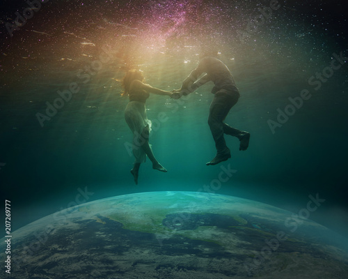 Surrealistic composition - a young man and a girl hovering over the globe under water