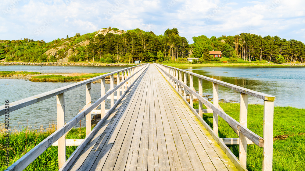 Long wooden pedestrian bridge in coastal landscape on a sunny evening.