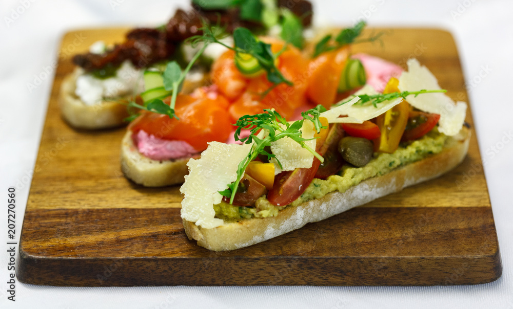three bruschettas on brown wooden board. With tomato, salmon and cheese