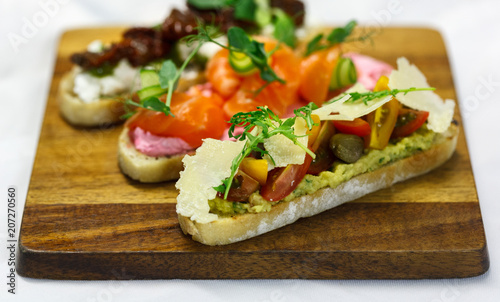 three bruschettas on brown wooden board. With tomato, salmon and cheese
