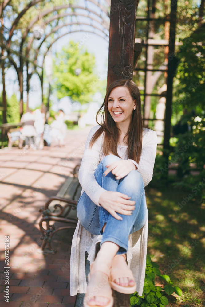 Portrait of beautiful caucasian young woman with charming smile wearing light casual clothes. Smiling female sitting under archway in city park in street outdoors on spring nature. Lifestyle concept. Portrait of beautiful caucasian young woman with charming smile wearing light casual clothes. Smiling female sitting under archway in city park in street outdoors on spring nature. Lifestyle concept.