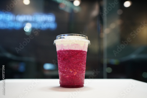 Plastic glass of pink dragon fruit smoothie with layer of cream cheese foam on blurred background, Traditional Taiwanese and Chinese Beverage.