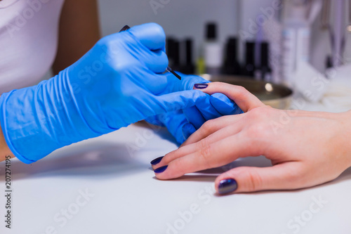 Professional beautician applying nail polish to female nail in a nail salon.