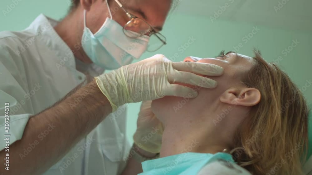 Dentist treats a tooth of female patient using dental equipment in office Dentist treats a tooth of female patient using dental equipment in office