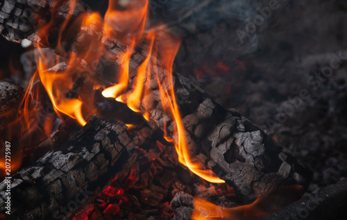 Fireplace with burning firewood and colorful flames on black background. Close up with details, space.