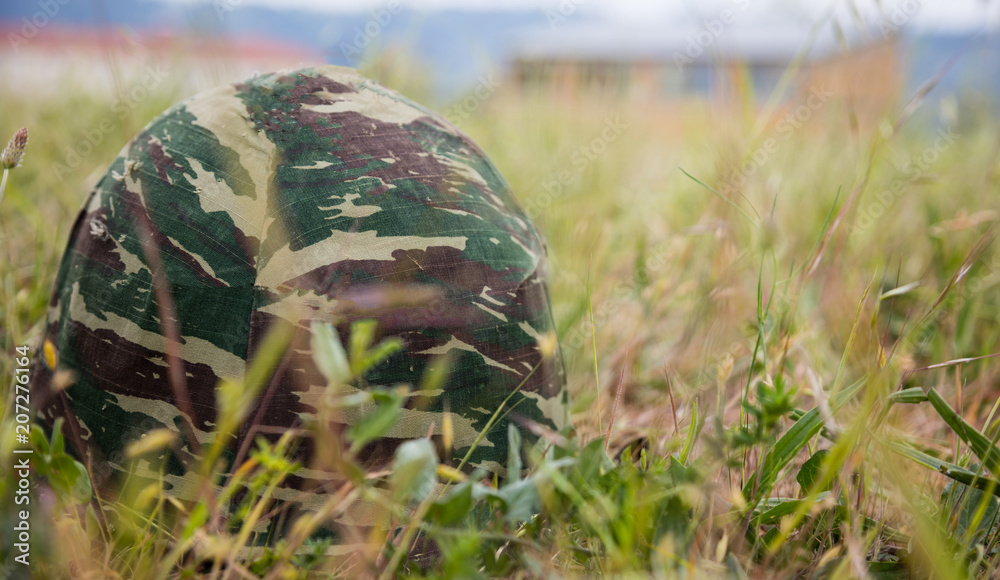 Fototapeta premium Army camouflage helmet putted down on the ground. Close up front view, blurred nature background, copyspace.