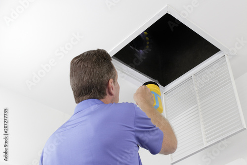 Man Inspecting an Air Duct with a Flashlight.Older male with a yellow flashlight examining HVAC ducts in a large square vent. Male technician looking over the air ducts inside a home air intake vent.