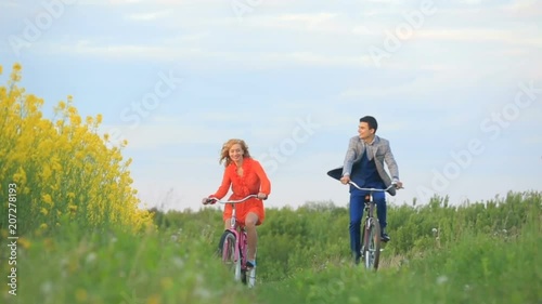 Front view of the beautiful cheerful co uple of lovers actively riding the bicycles along the green blooming field. photo