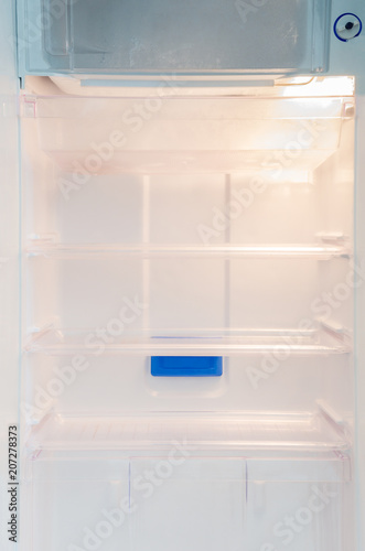 Opened and empty inside white refrigerator background of regular cool shelf and frozen section for storing food, fruits, drinks, vegetables, with light on and button for temperature adjustment