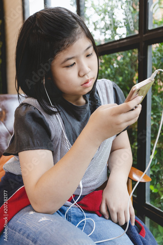 Asian little girl black hair. holding playing smartphone listen to music