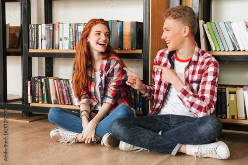 Smiling teenage couple sitting on a floor at the bookshelf