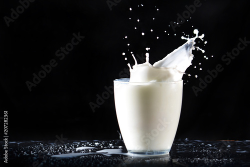 Abundant milk splashes of glass transparent glass, flying in all directions, falling on the table on a black background.