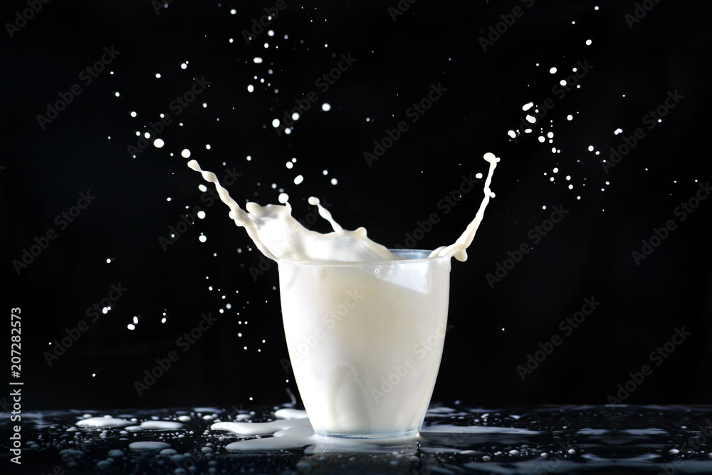 Milk splashes from a glass transparent glass, flying in all directions, falling on the table on a black background.
