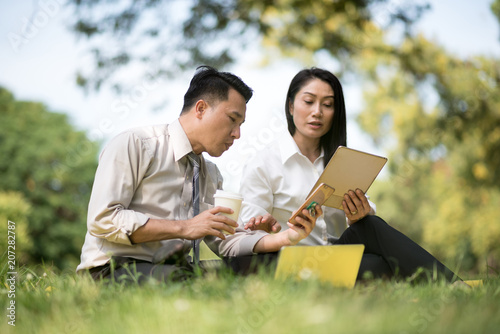 Selective focus business couple relaxing with tablets in park after work done