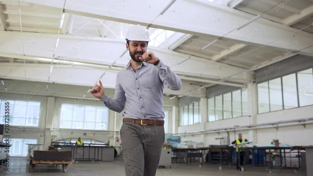 Portrait of adult happy man, head director or engineer, wearing suit and helmet rejoicing and dancing while walking though manufacture slow motion Portrait of adult happy man, head director or engineer, wearing suit and helmet rejoicing and dancing while walking though manufacture slow motion