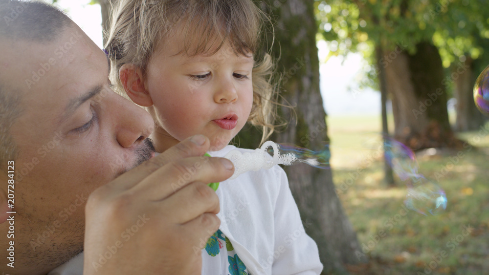 CLOSE UP: Proud dad and his cute little daughter blowing bubbles in the park. CLOSE UP: Proud dad and his cute little daughter blowing bubbles in the park.