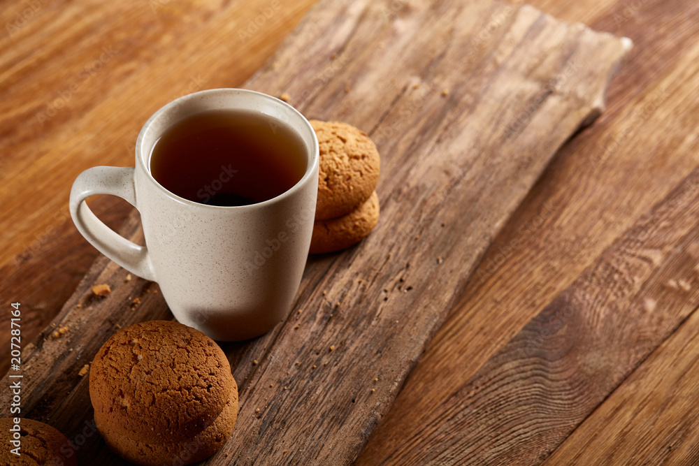 White porcelain mug of tea and sweet cookies on piece of wood over wooden background, top view, selective focus White porcelain mug of tea and sweet cookies on piece of wood over wooden background, top view, selective focus