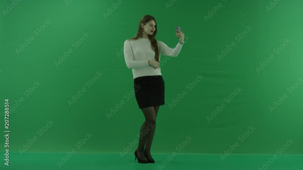 girl is standing in a half-turn, looking at the right and making a selfie on green screen girl is standing in a half-turn, looking at the right and making a selfie on green screen