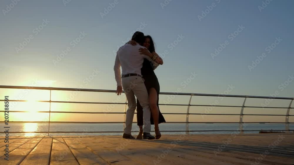 Dance latina performed by a professional couple in slow motion on sea beach. Woman in sexual black dress. Sensual salsa, bachata, rumba.