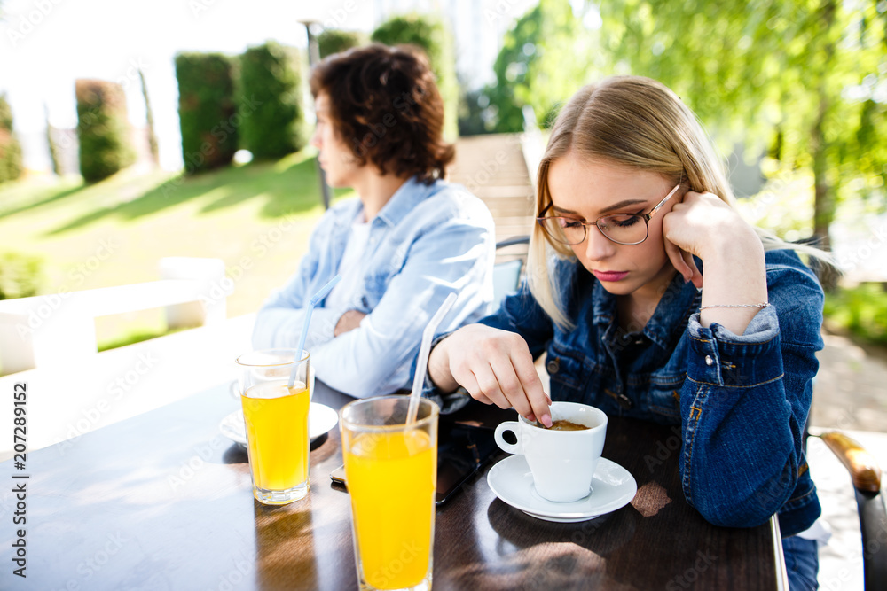 Young upset couple sitting side by side at cafe's garden Young upset couple sitting side by side at cafe's garden