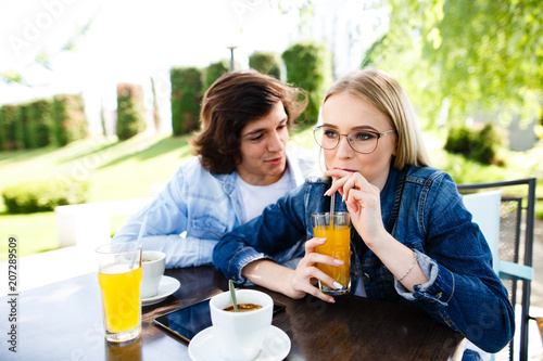 Young romantic couple spending time together - sitting in cafe's garden, drinking juice and having fun