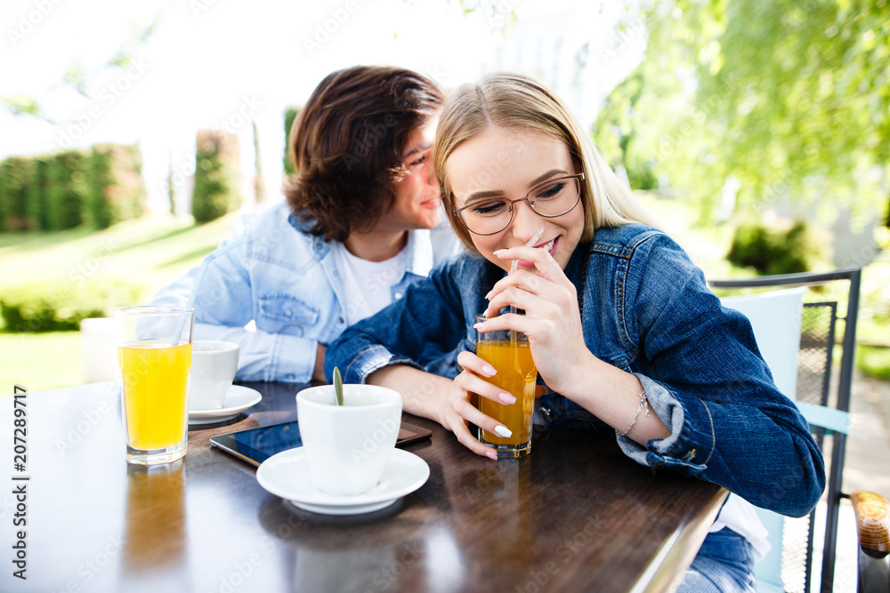 Young romantic couple spending time together - sitting in cafe's garden, drinking juice and having fun Young romantic couple spending time together - sitting in cafe's garden, drinking juice and having fun