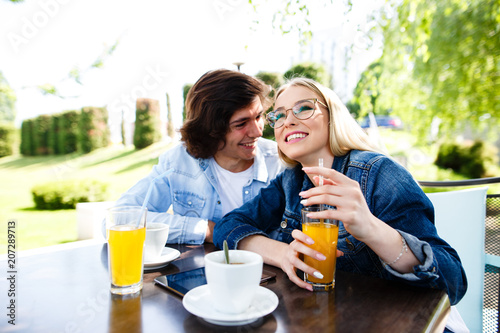 Young romantic couple spending time together - sitting in cafe's garden, drinking juice and having fun