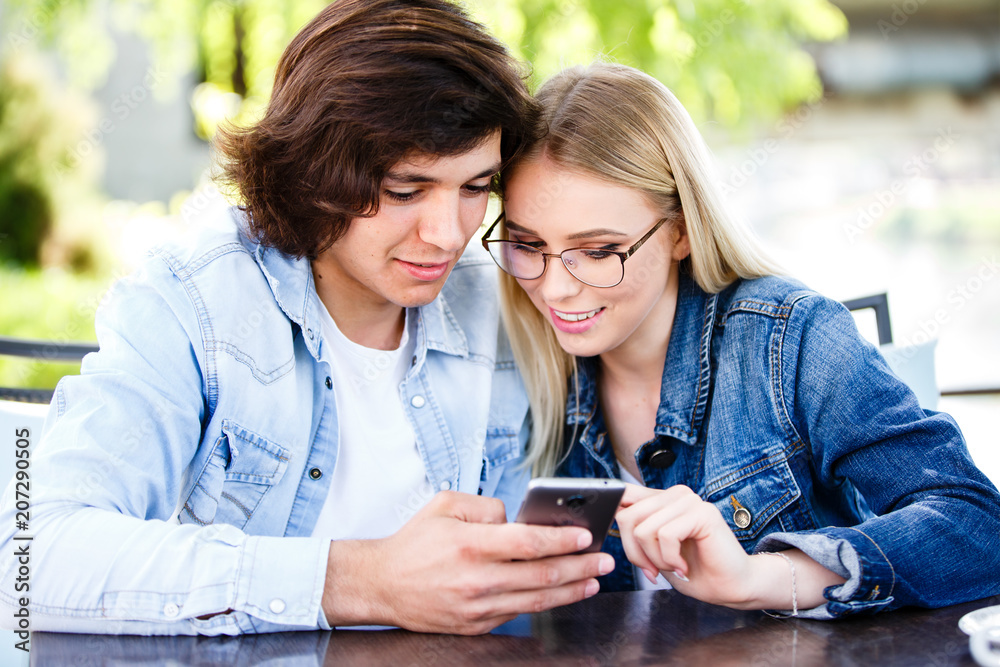 Couple spending valentines day on social networks, using phone device while sitting together at cafe