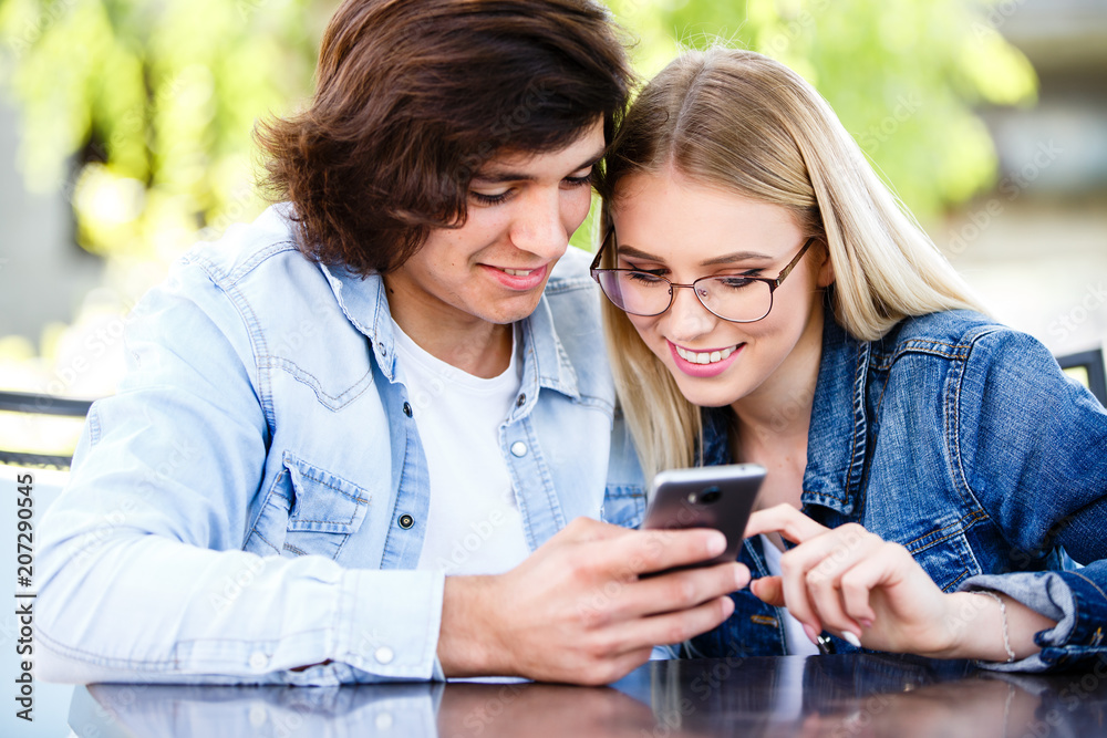 Couple spending valentines day on social networks, using phone device while sitting together at cafe Couple spending valentines day on social networks, using phone device while sitting together at cafe