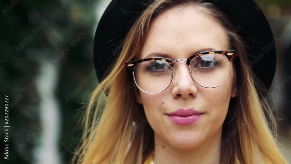 Young woman with black hat and glasses in sunny spring town.