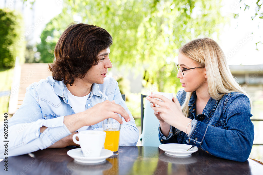 Young romantic couple spending time together - sitting in cafe's garden, drinking beverage Young romantic couple spending time together - sitting in cafe's garden, drinking beverage