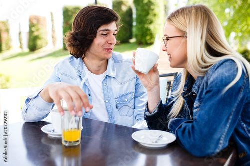 Young romantic couple spending time together - sitting in cafe's garden, drinking beverage