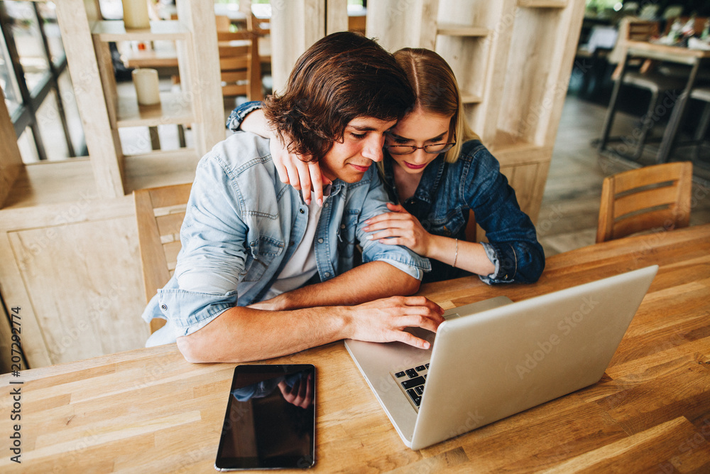 Young charming couple using laptop while sitting at cafe Young charming couple using laptop while sitting at cafe