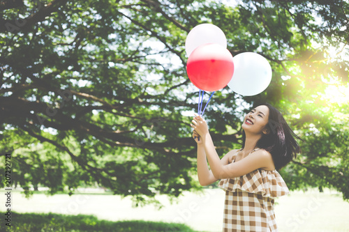 A beautiful woman has joyful and feels happiness. Pretty girl holds balloons and gorgeous beautiful woman retrospect in the past when she was child. Lovely girl is enjoying life with park background