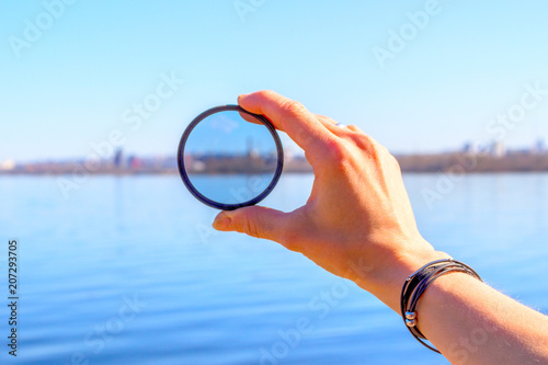 Female hand with a photo filter on the background of the lake and the city