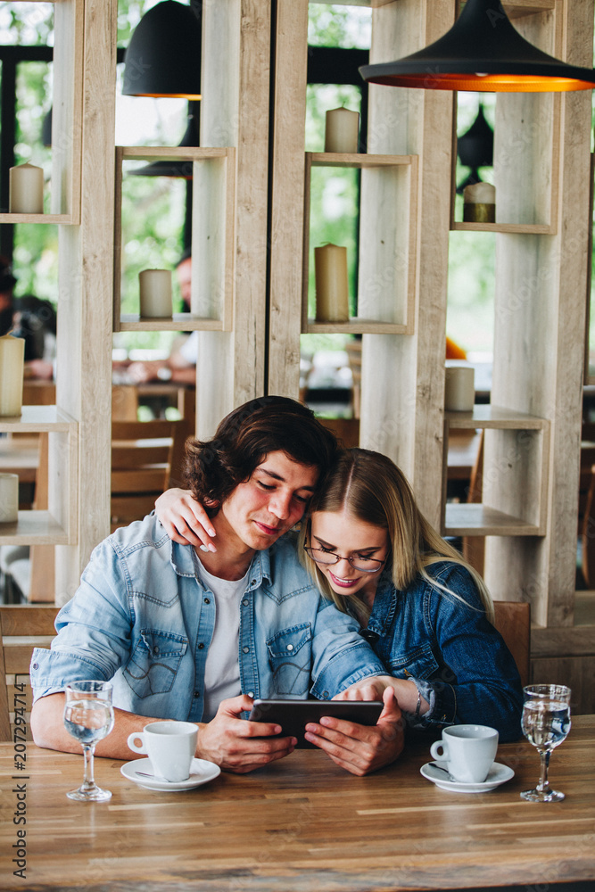 Young Charming Couple Using Tablet While Sitting Together And Drinking Coffee Young Charming Couple Using Tablet While Sitting Together And Drinking Coffee