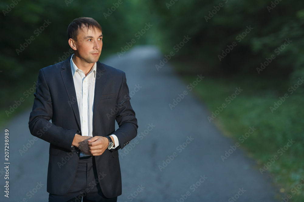 Handsome young man in a business suit walking on a forest road Handsome young man in a business suit walking on a forest road