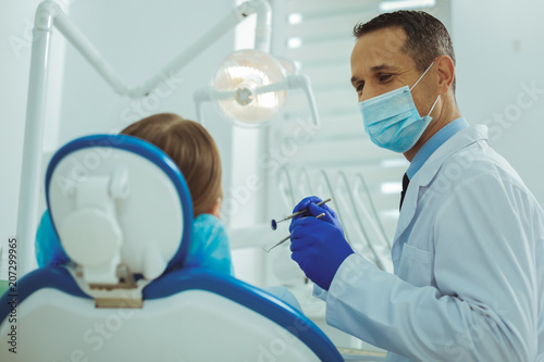 Good mood. Professional dentist holding instrument while examining his patient