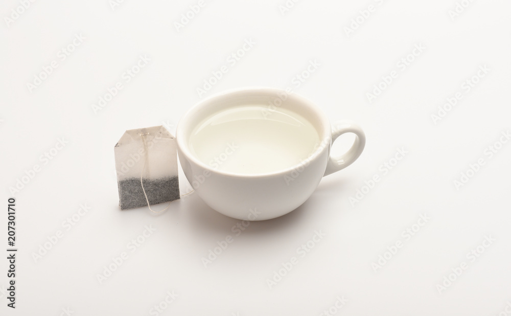 Mug filled with boiling water and teabag on white background. Process of tea brewing in ceramic mug. Tea time concept. Cup or white porcelain mug with transparent hot water and dry bag of tea near Mug filled with boiling water and teabag on white background. Process of tea brewing in ceramic mug. Tea time concept. Cup or white porcelain mug with transparent hot water and dry bag of tea near