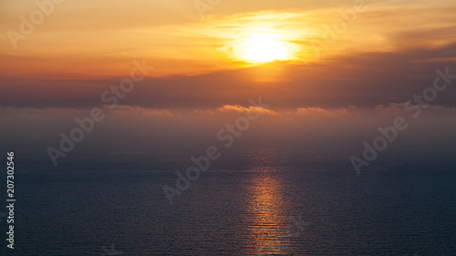  The sun is above the ocean behind beautiful clouds.