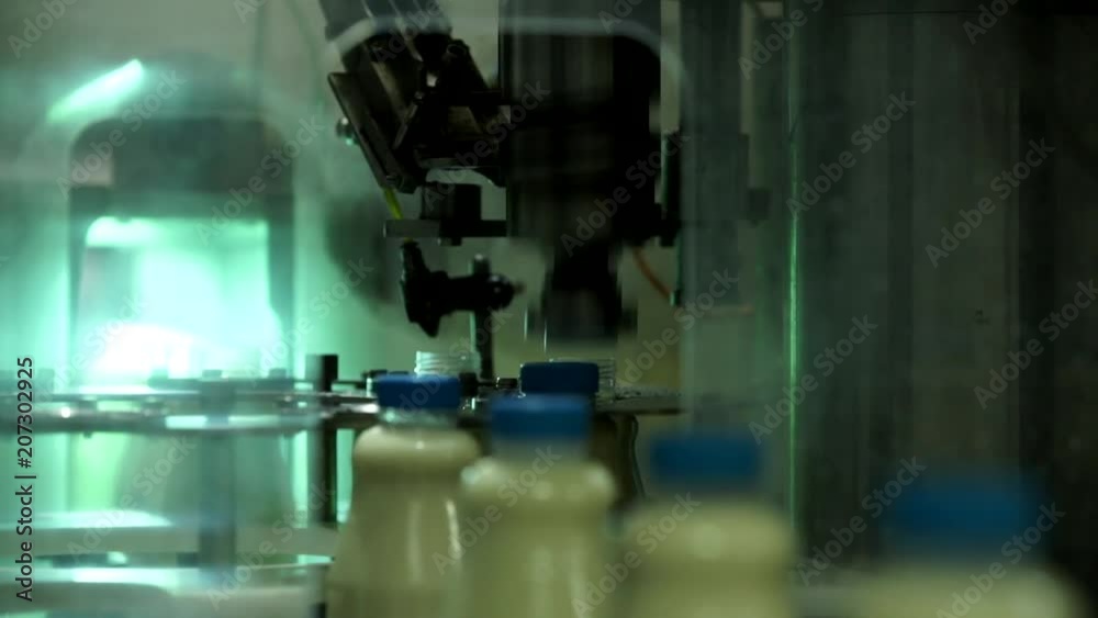The automatic device spins the bottle cap. Automated line for the production of milk in plastic bottles. Milk bottles on a conveyor belt. The automatic device spins the bottle cap. Automated line for the production of milk in plastic bottles. Milk bottles on a conveyor belt.