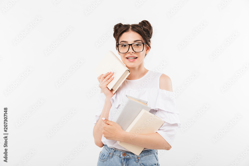 Photo of european teenage girl 20s with double buns hairstyle and dental braces smiling and holding many studying books, isolated over white background Photo of european teenage girl 20s with double buns hairstyle and dental braces smiling and holding many studying books, isolated over white background