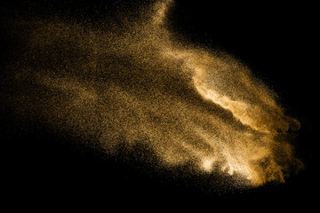 Golden sand explosion isolated on black background. Abstract sand cloud. Golden colored sand splash against dark background. Yellow sand fly wave in the air.